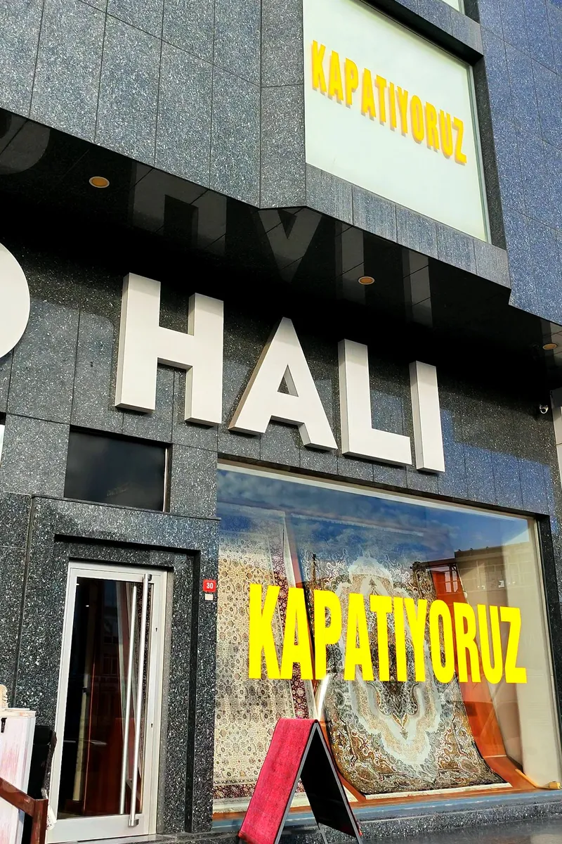 MD Halı mağazasının Avcılar E-5 üzerindeki granit cephesi; vitrinlerde sarı harflerle KAPATIYORUZ yazıyor