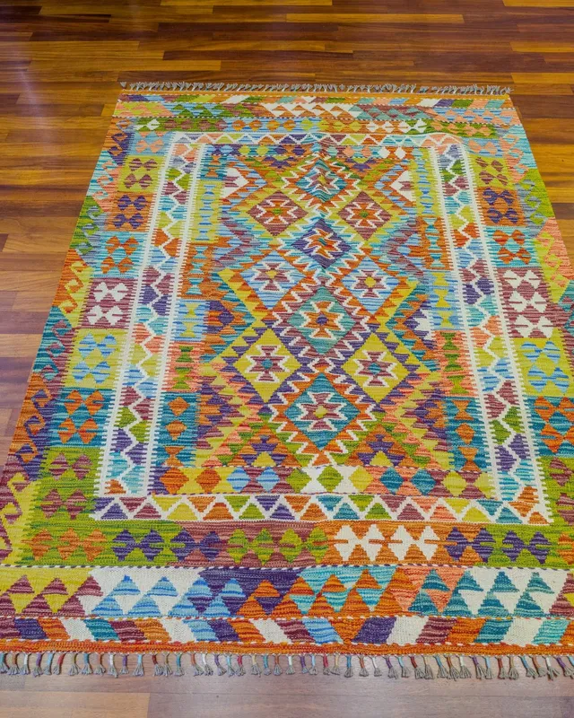 Ahşap zemine serili, turuncu, yeşil, mor ve mavi tonlarda baklava zincirli, renkli püsküllü kilim
