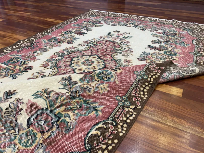 Ahşap zemine serili, krem zeminli, pembe ve bordo tonlarda çiçek desenli vintage el dokuma halı