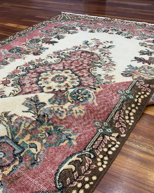 Ahşap zemine serili, krem zeminli, pembe ve bordo tonlarda çiçek desenli vintage el dokuma halı